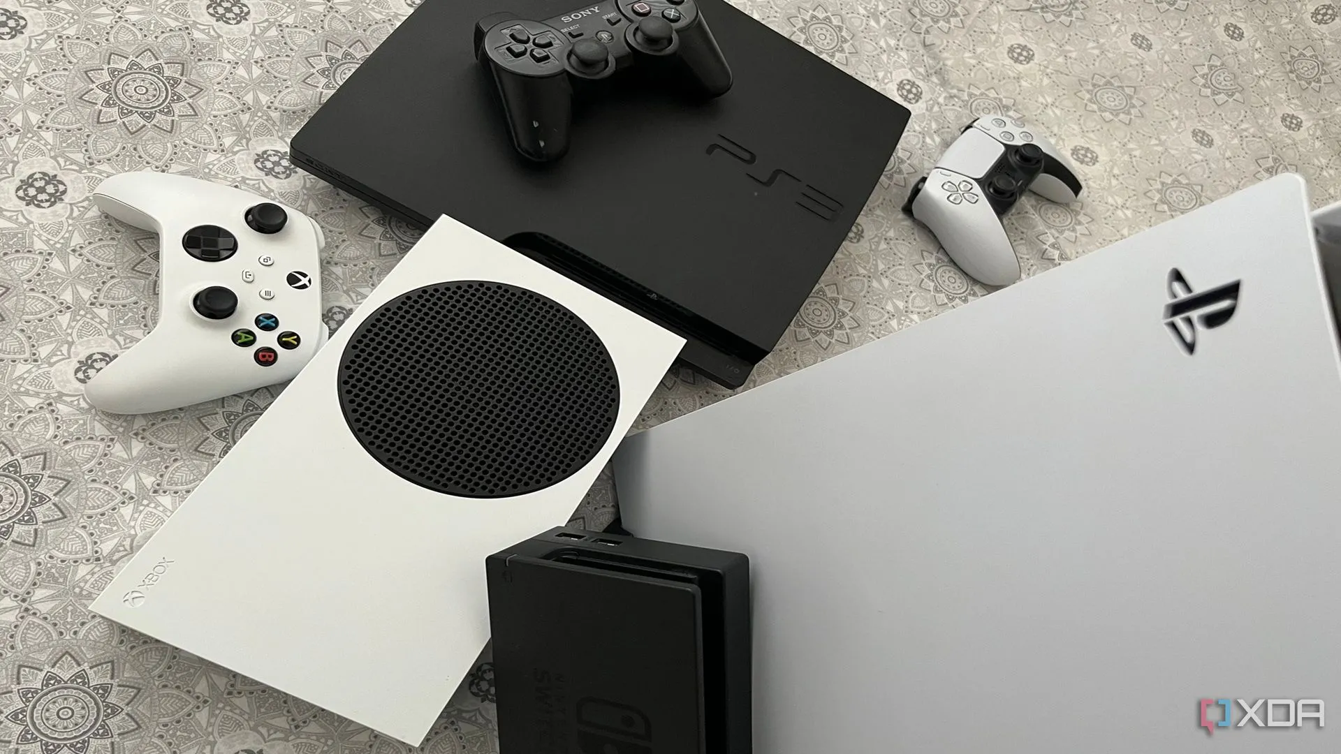 Bộ sưu tập các máy chơi game bao gồm PS5, Xbox Series X, dock Switch và PS3, thể hiện sự đa dạng cấu hình phần cứng
