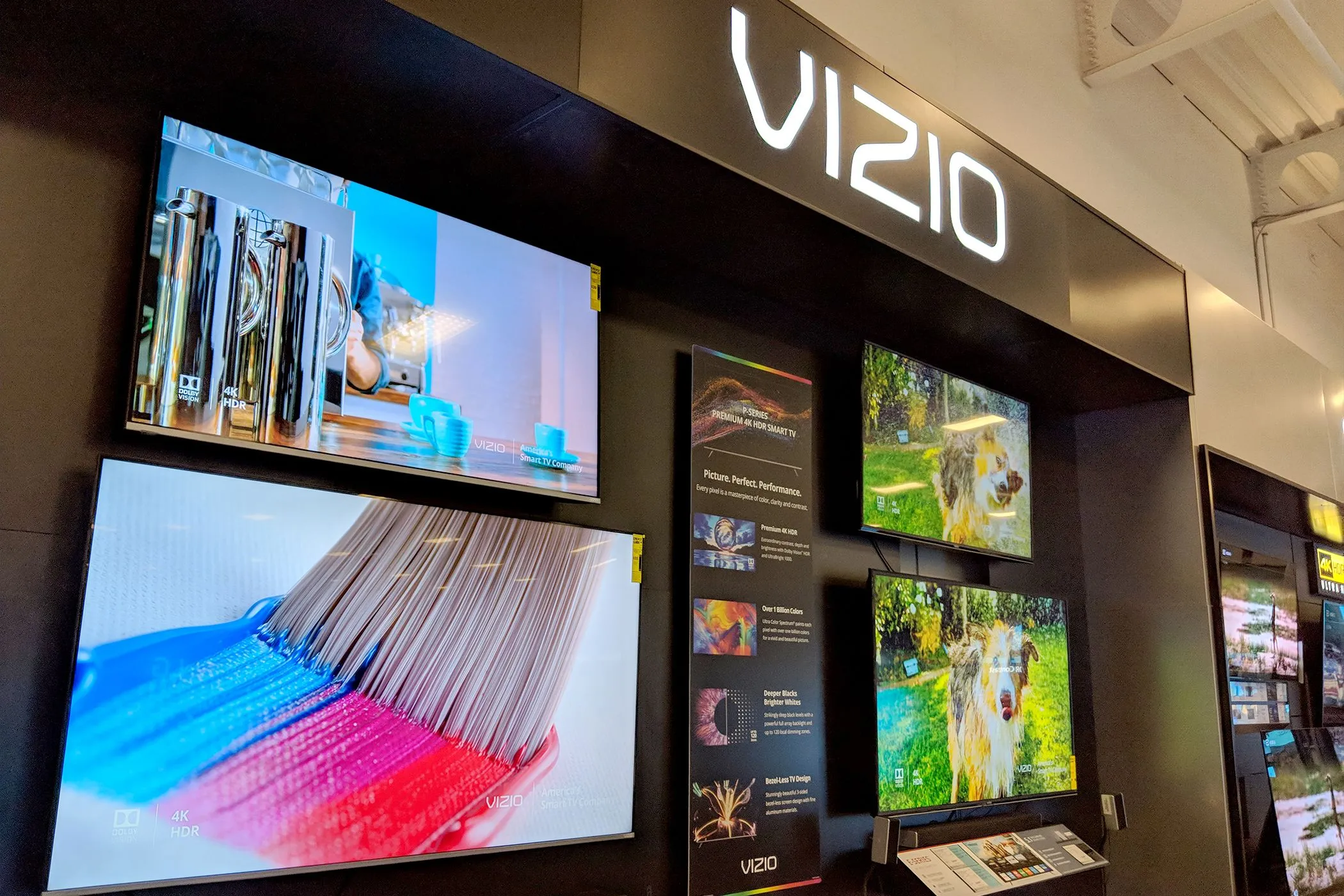 Dãy TV Vizio được trưng bày tại cửa hàng bán lẻ điện tử, minh họa đa dạng mẫu mã và kích cỡ.