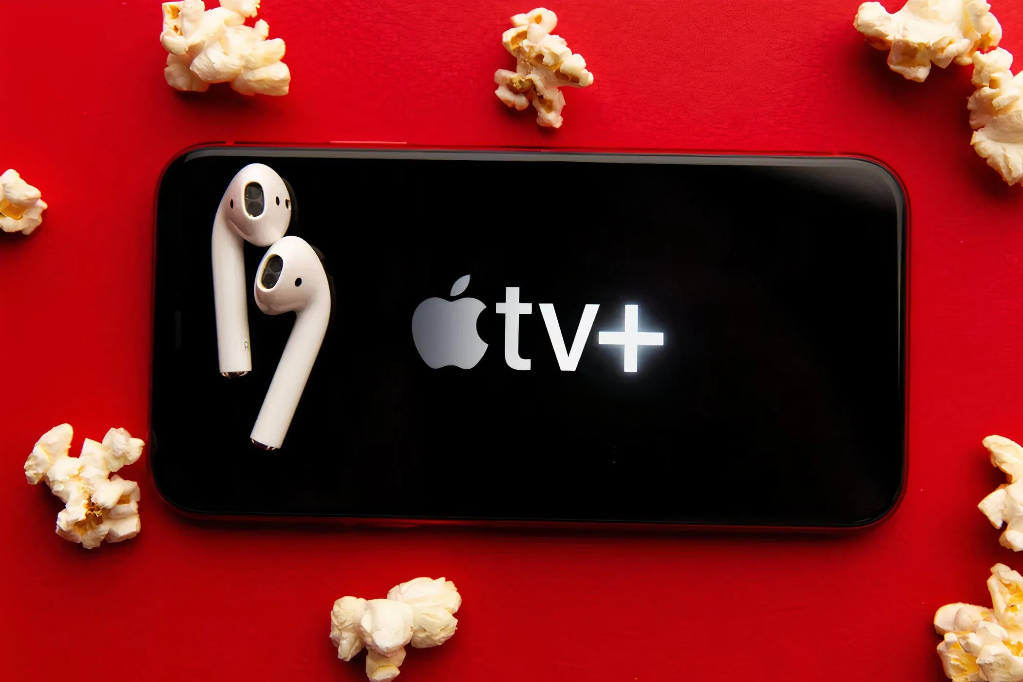 Màn hình điện thoại hiển thị logo Apple TV+, xung quanh là bắp rang bơ và tai nghe, biểu tượng cho trải nghiệm xem phim giải trí di động tiện lợi.