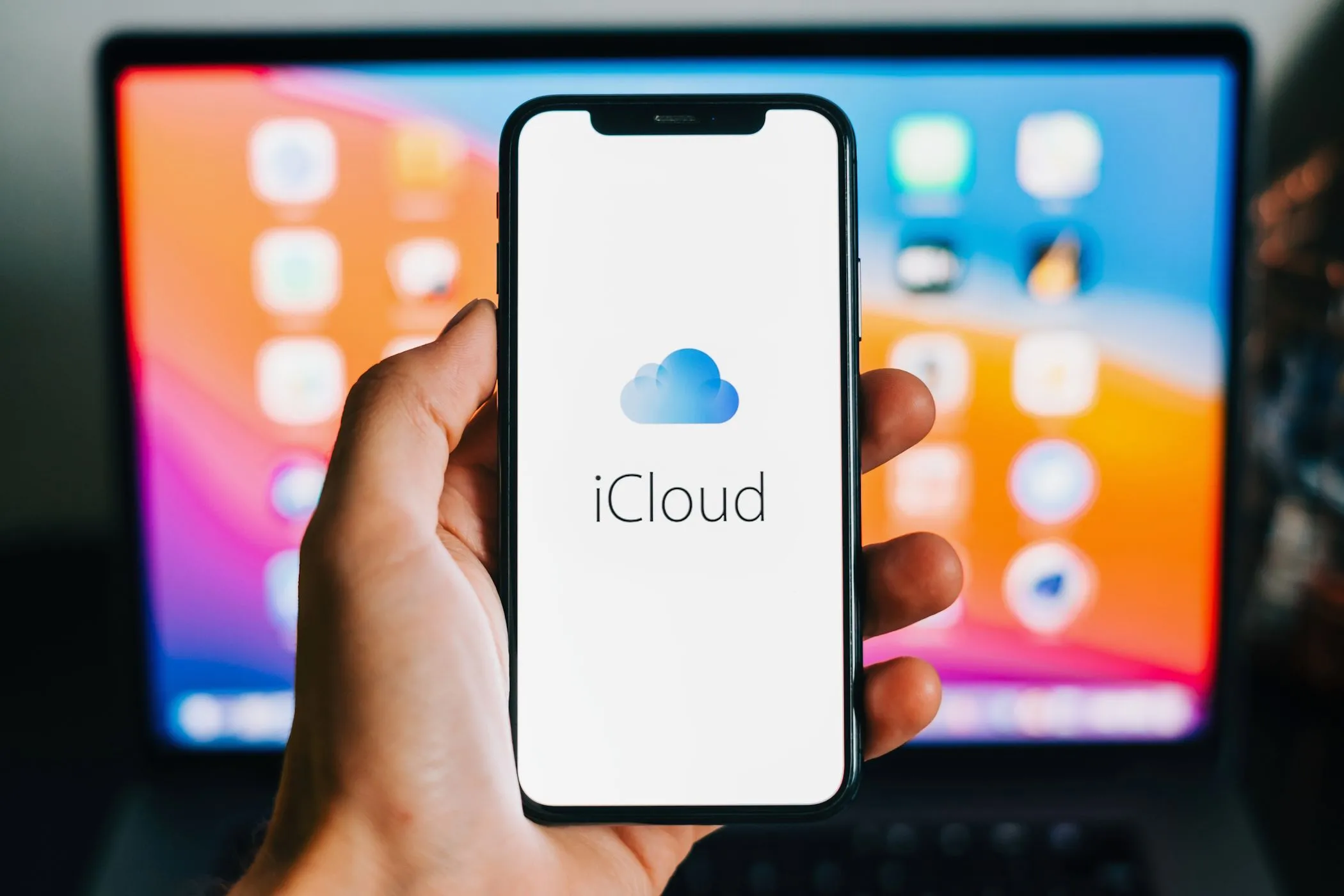 Biểu tượng iCloud xuất hiện trên màn hình iPhone, phía sau là MacBook