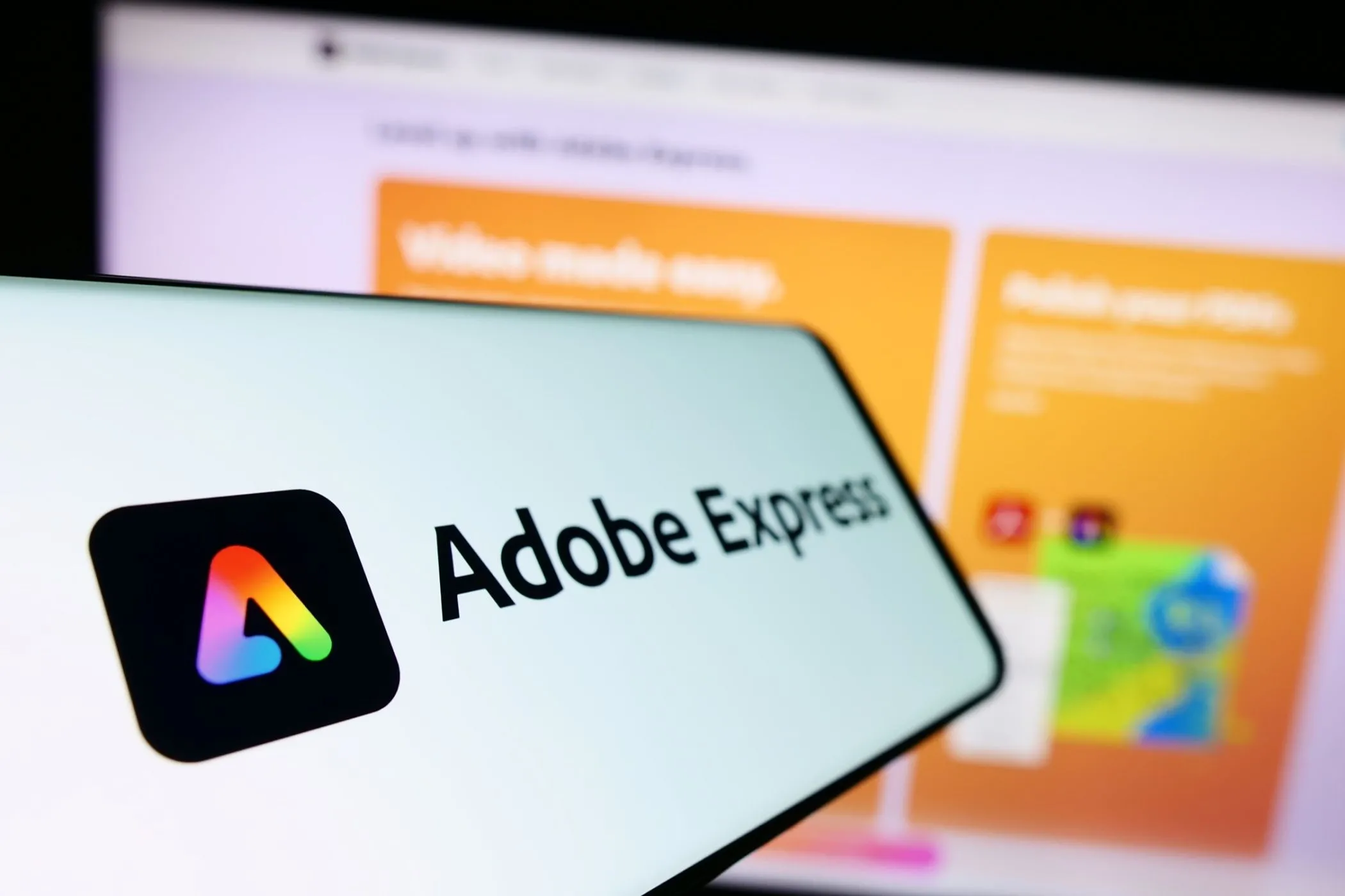 Điện thoại hiển thị logo Adobe Express với thiết kế đồ họa máy tính phía sau