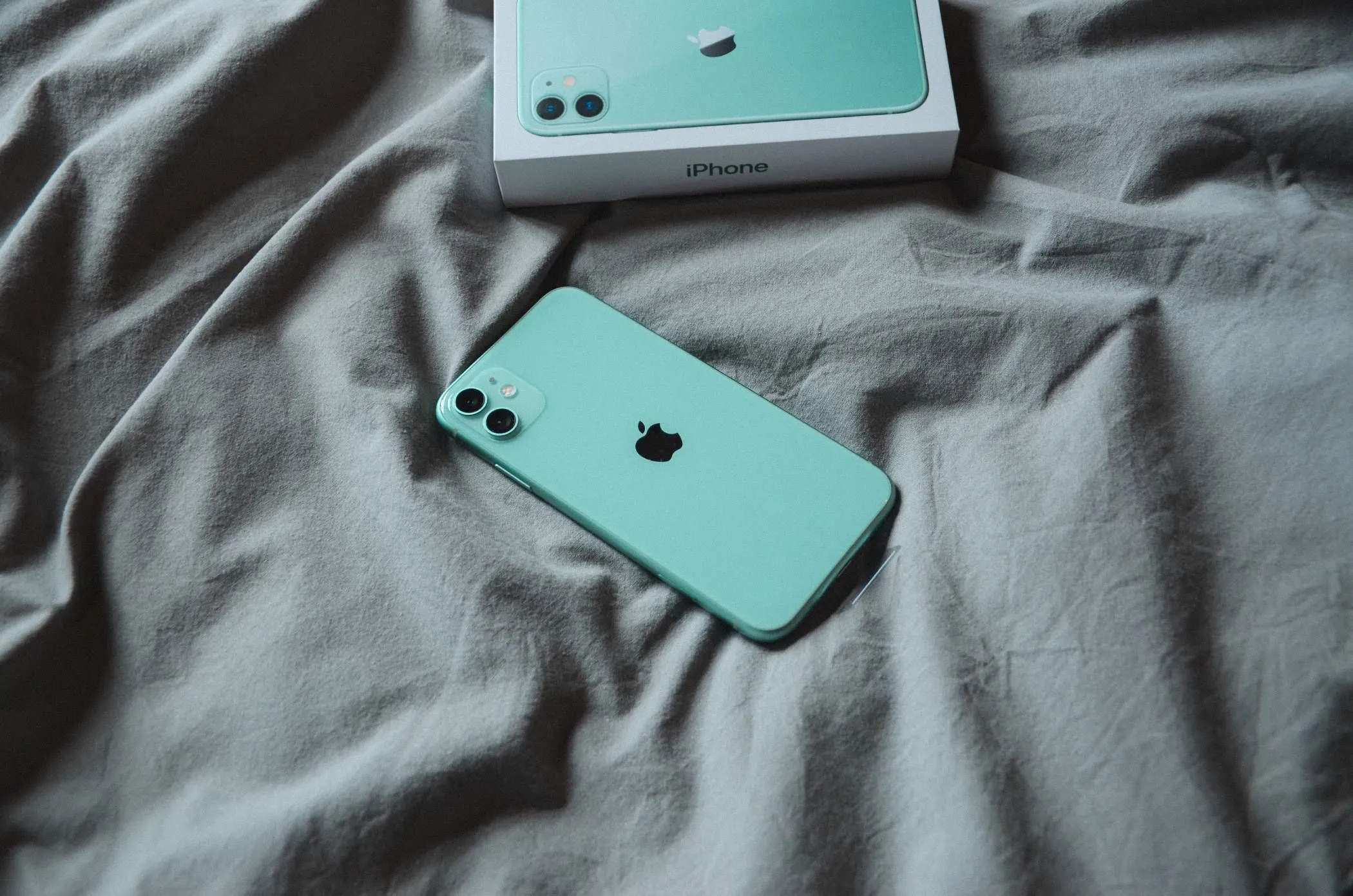 iPhone đặt trên chăn ga giường đang sạc, cảnh báo nguy cơ nóng máy và hỏa hoạn.