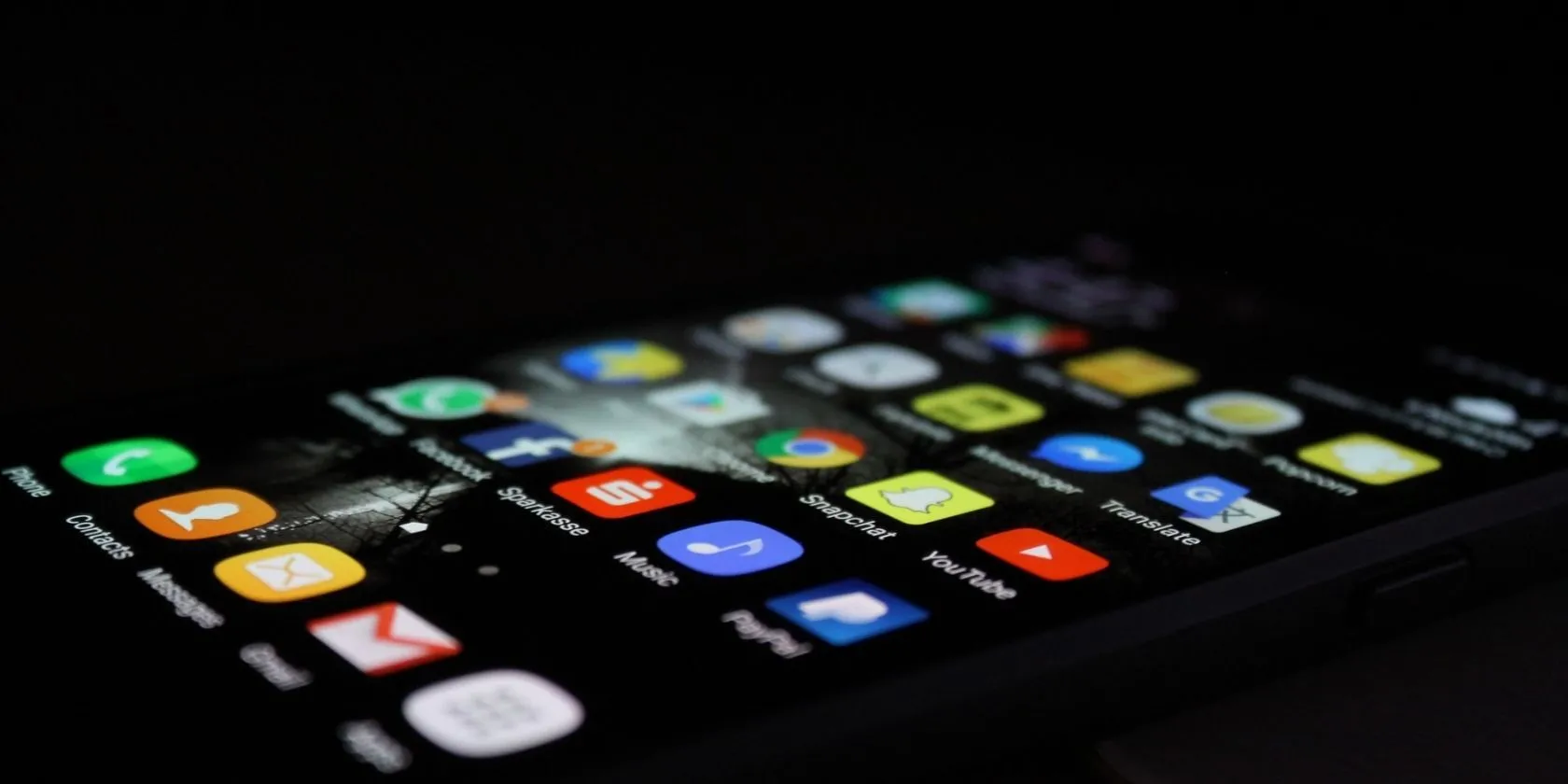 iPhone màu đen nằm úp với các ứng dụng trên màn hình chính trên nền tối