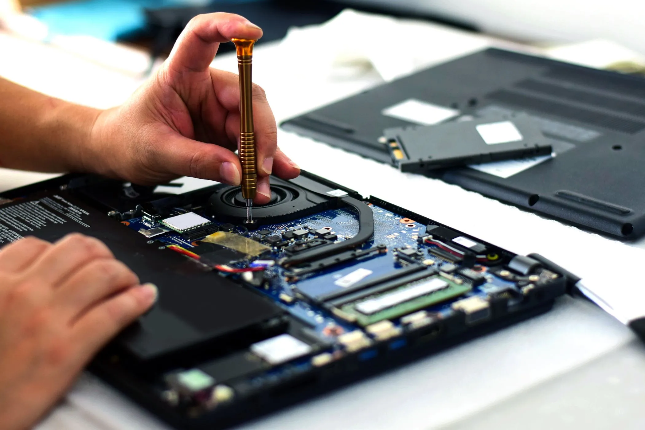 Kỹ thuật viên đang sử dụng tuốc nơ vít để sửa bo mạch chủ của laptop, nhấn mạnh vấn đề khó sửa chữa của các mẫu máy mỏng nhẹ.