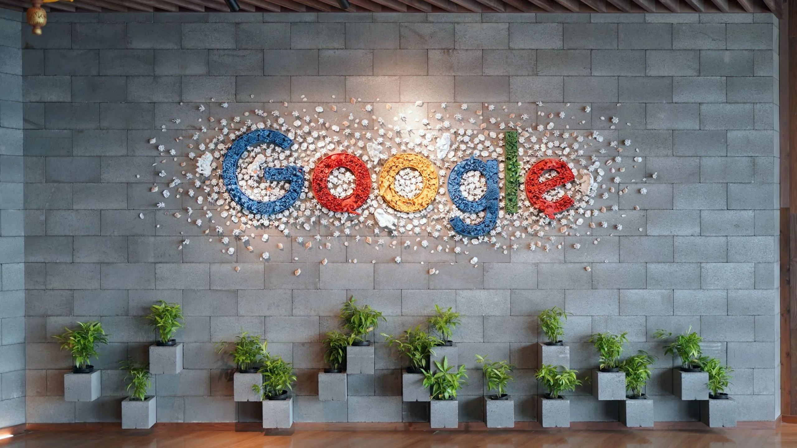 Logo Google trên tường văn phòng có cây xanh, tượng trưng cho sự tích hợp sâu rộng của Chromebook với hệ sinh thái Google và khả năng đồng bộ liền mạch.