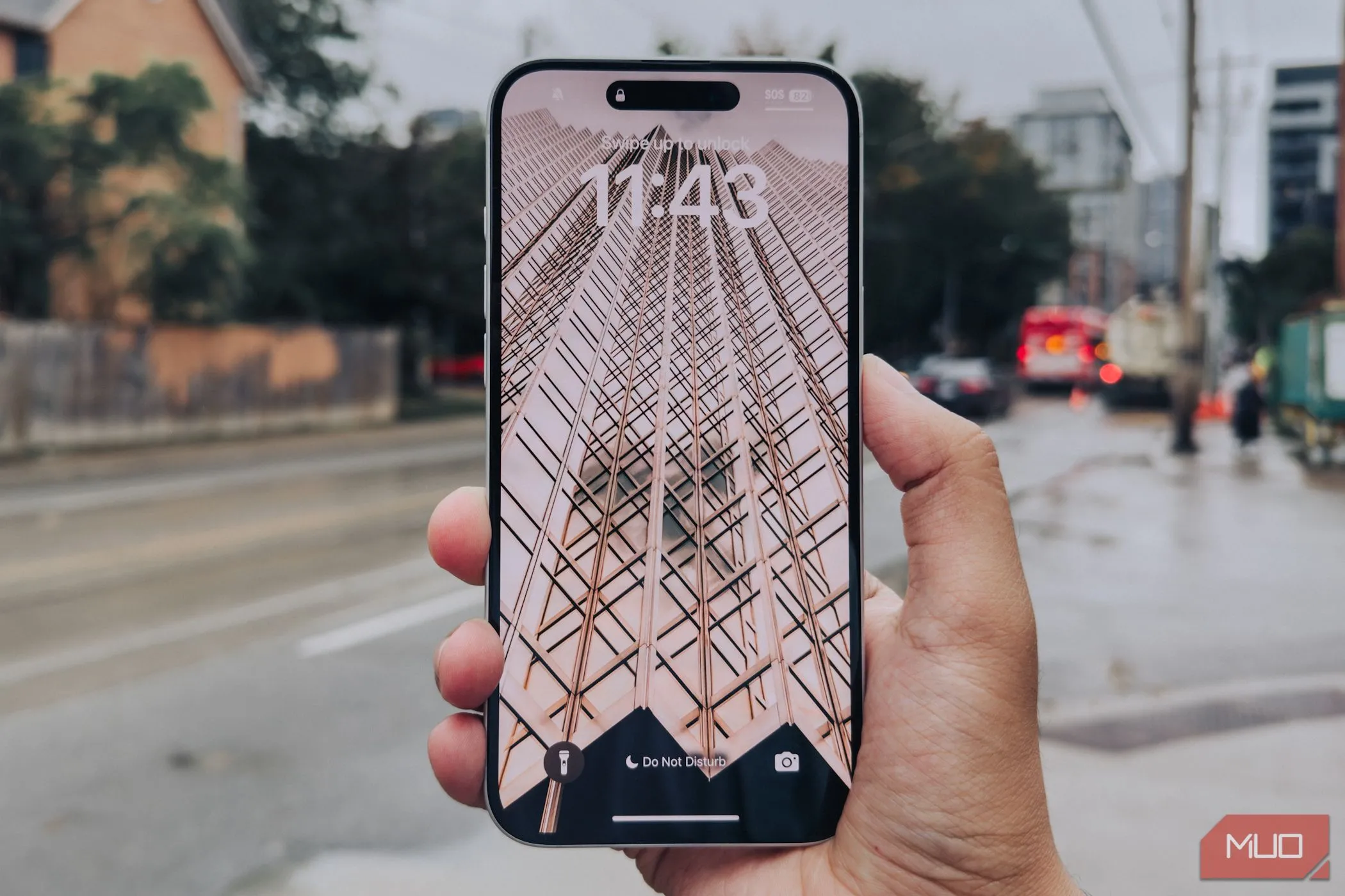 Màn hình iPhone 16 Plus với viền mỏng được cầm trên tay trước cảnh thành phố