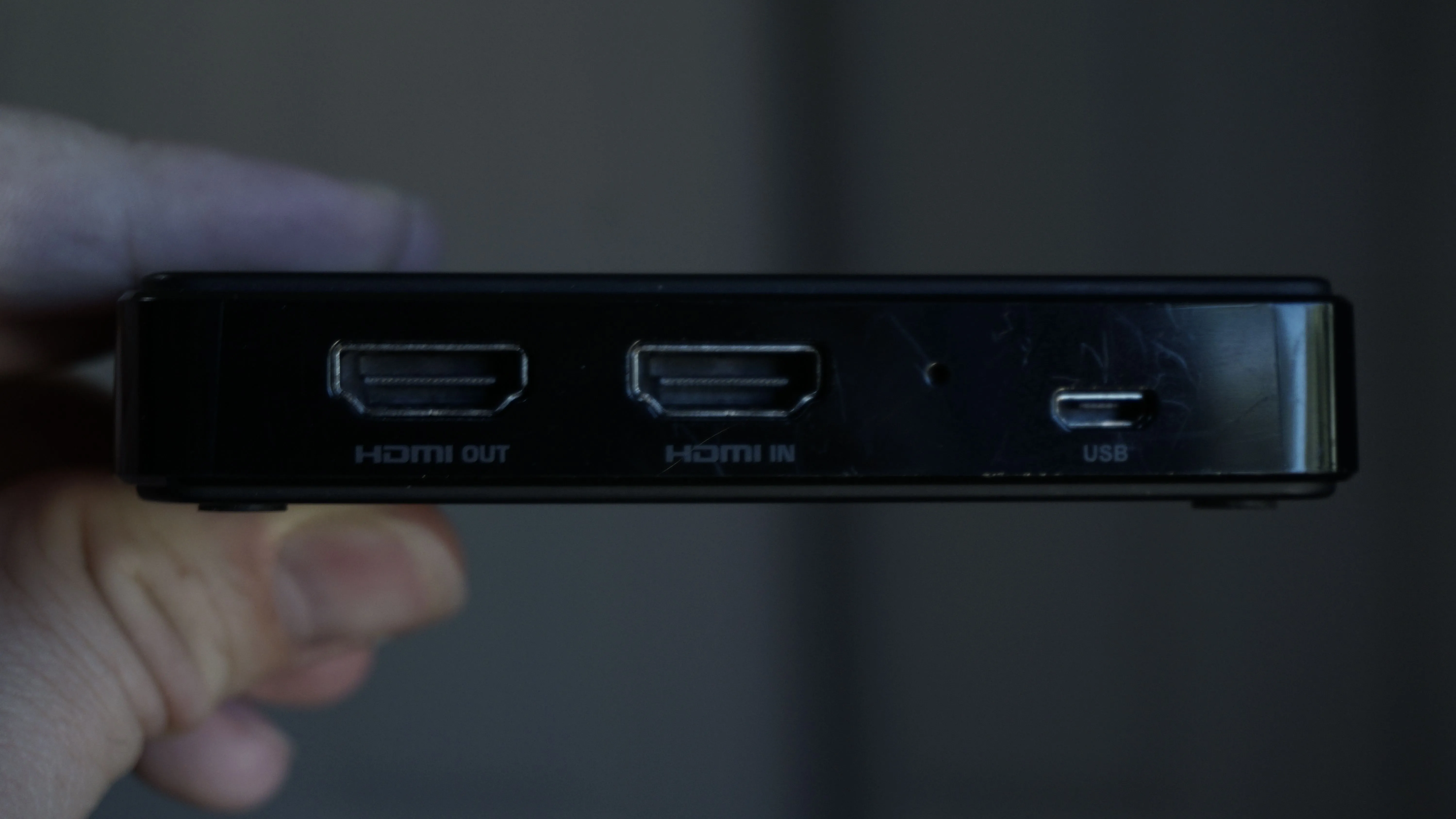 Một bàn tay đang cầm một card thu hình, hiển thị các cổng HDMI in/out và USB.