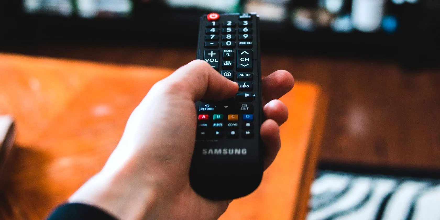 Một người đang sử dụng điều khiển từ xa để thay đổi kênh TV, minh họa khả năng điều khiển thiết bị qua tính năng hồng ngoại của điện thoại.