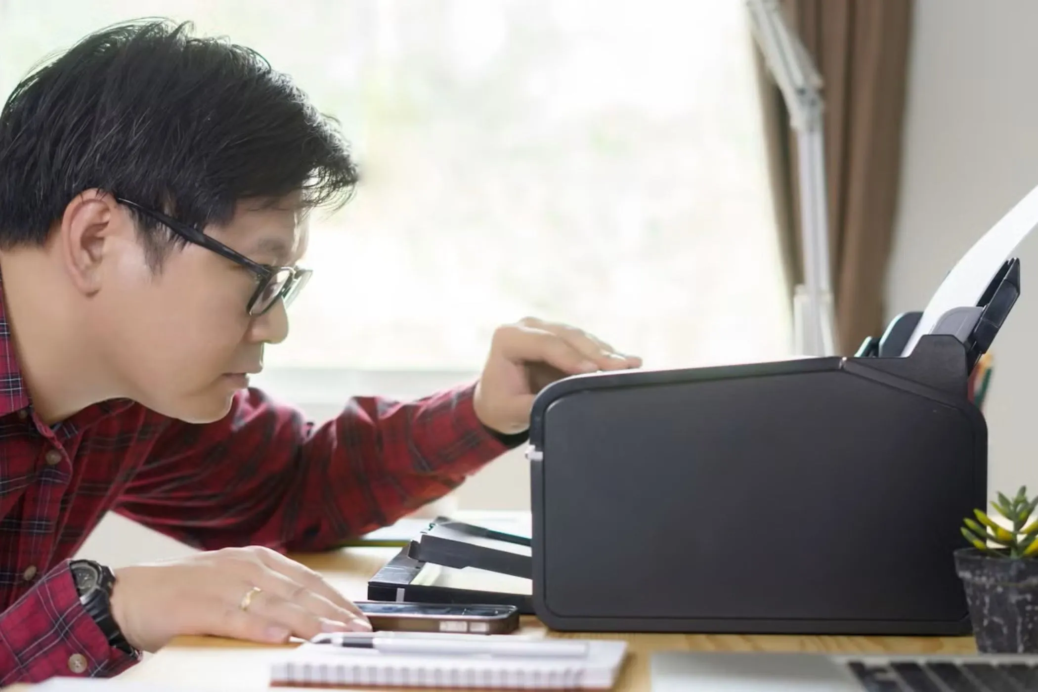 Người đàn ông đang nhìn vào máy in trên bàn làm việc, thể hiện sự tương thích của thiết bị ngoại vi