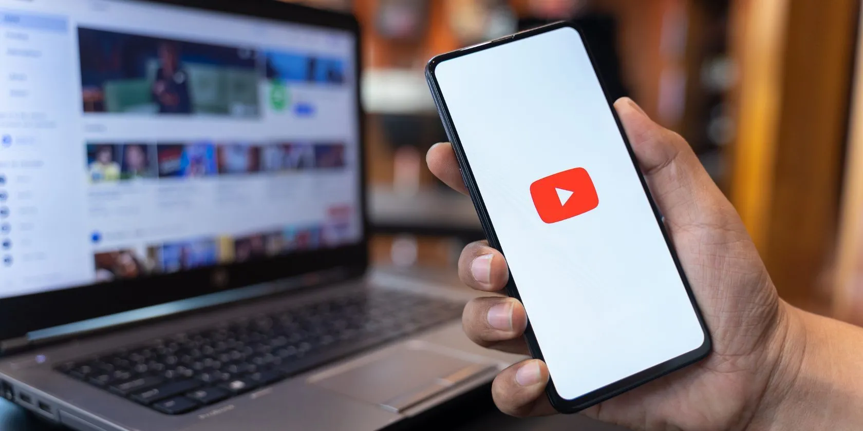 Người dùng cầm điện thoại với ứng dụng YouTube và trang web YouTube ở hậu cảnh