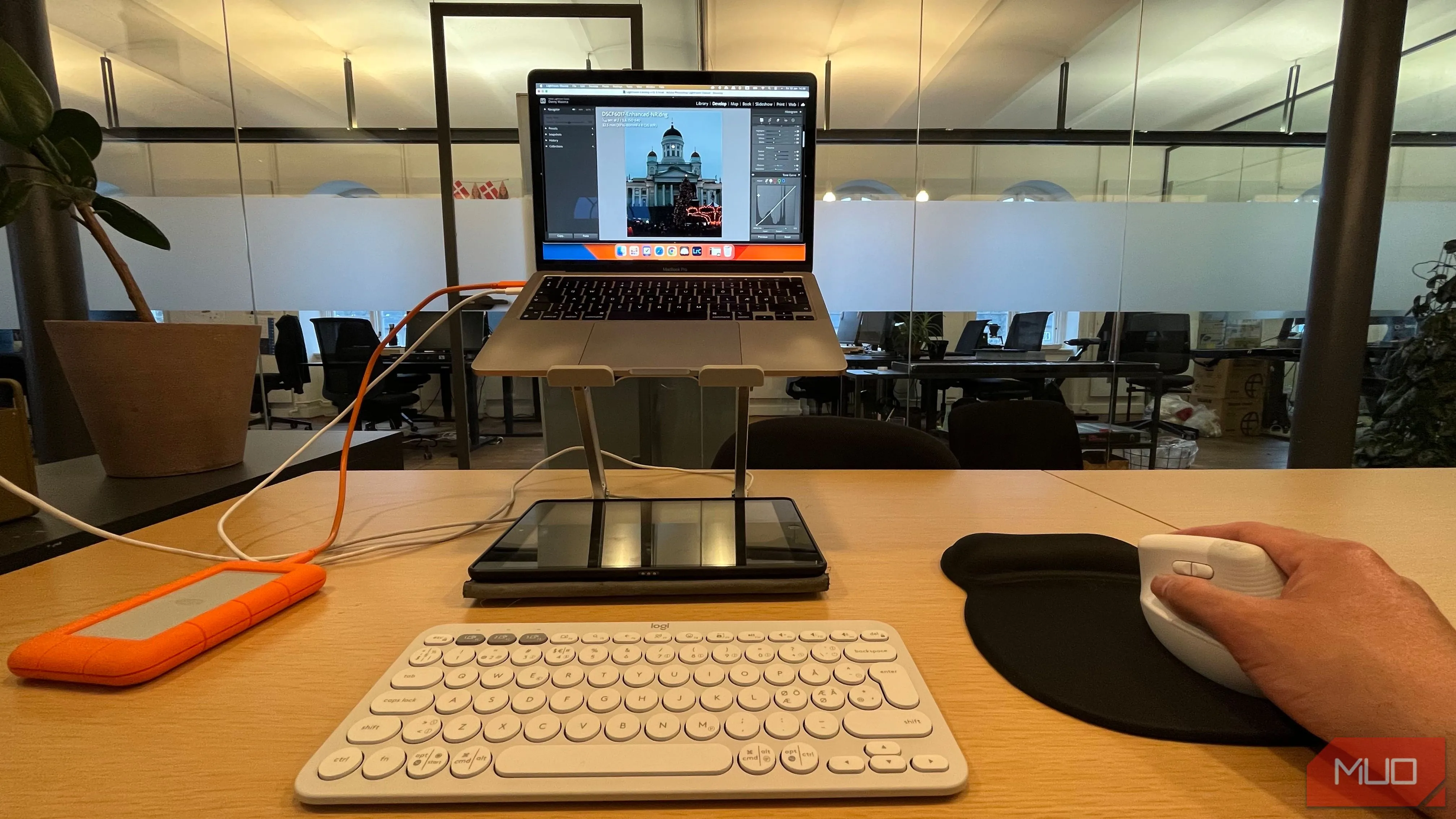 Người dùng chỉnh sửa ảnh trên laptop đặt trên giá đỡ, sử dụng chuột không dây