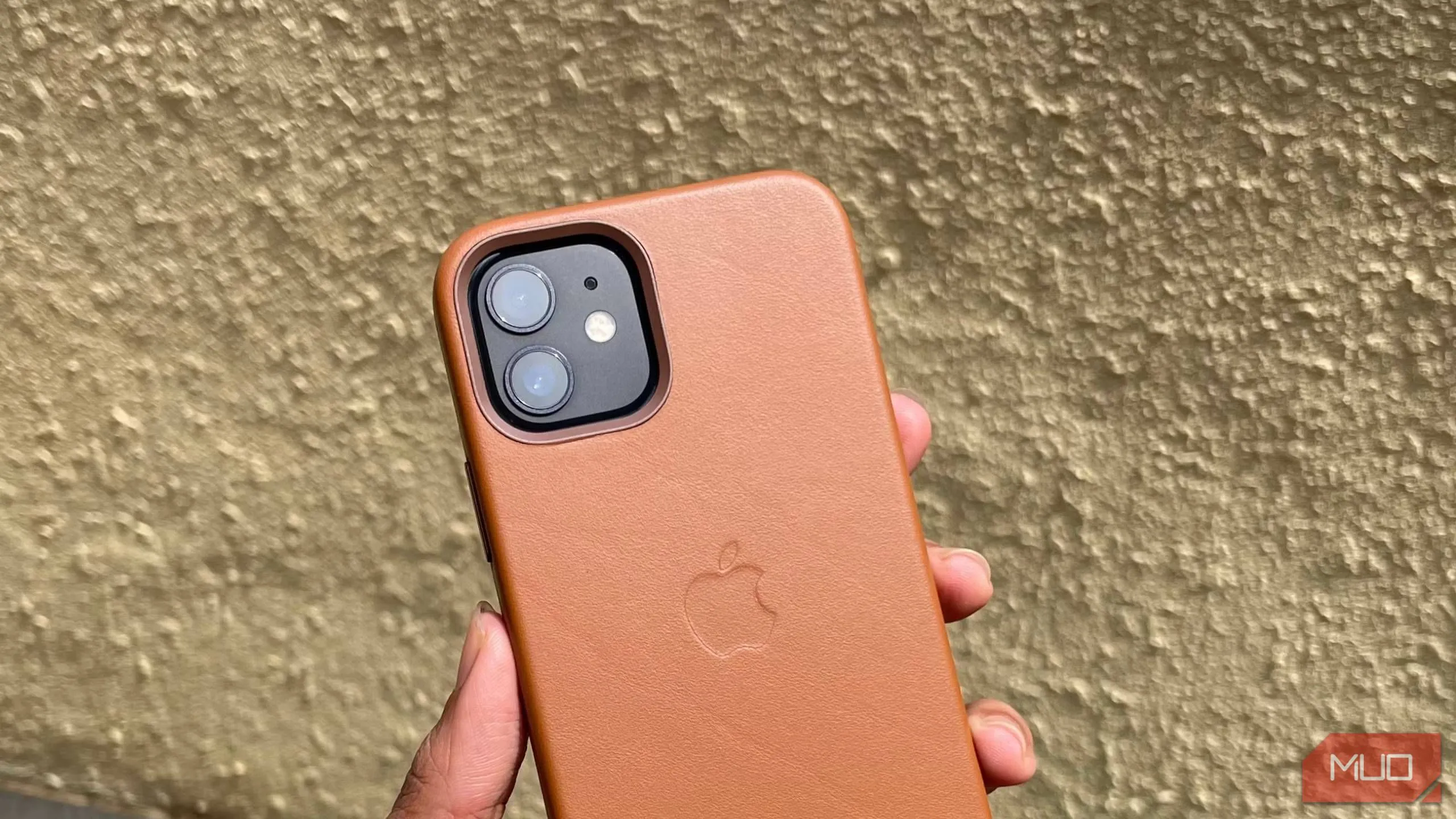 Người dùng đang cầm điện thoại iPhone 12 trong ốp lưng da màu nâu nhạt