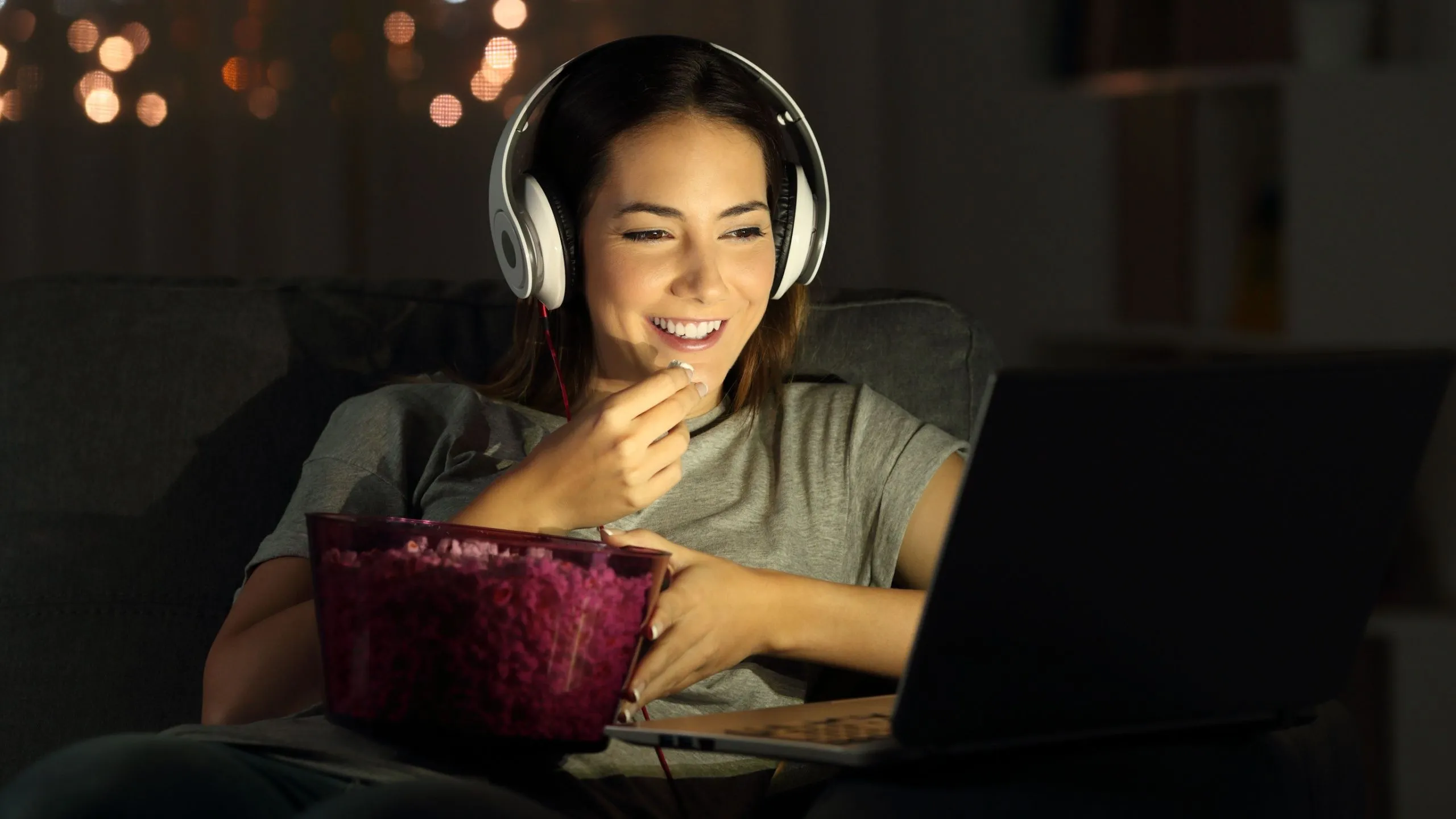 Người phụ nữ thư giãn xem phim trên laptop với bỏng ngô và tai nghe, trải nghiệm giải trí Netflix